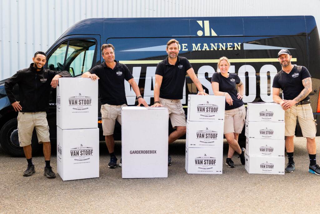 Het team van De Mannen van Stoof voor de verhuiswagen met verhuisdozen